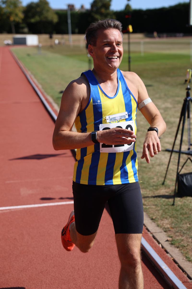Gareth Hiron smiling as he runs on a track in his club vest
